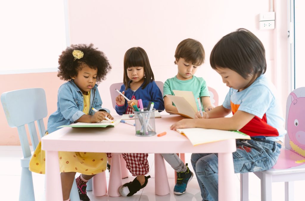 Cute Diverse children with kindergarten doing a creativity drawing at table indoors in classroom.