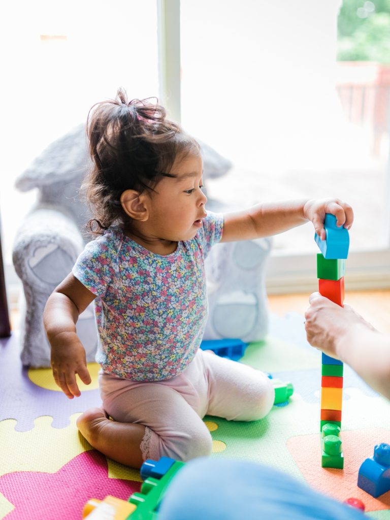 Diverse toddler girl at one happily playing with mega building blocks